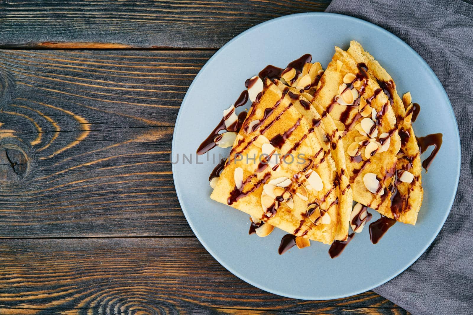 Two pancakes with chocolate syrup, almond flakes on plate, honey flows from spoon, top view, copy space