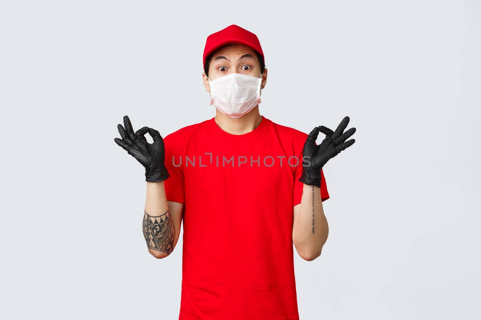 Worried young asian delivery man trying calm down nervous client, showing zen gesture, wearing medical mask and protective gloves, company uniform. Courier make okay sign ensure best quality.