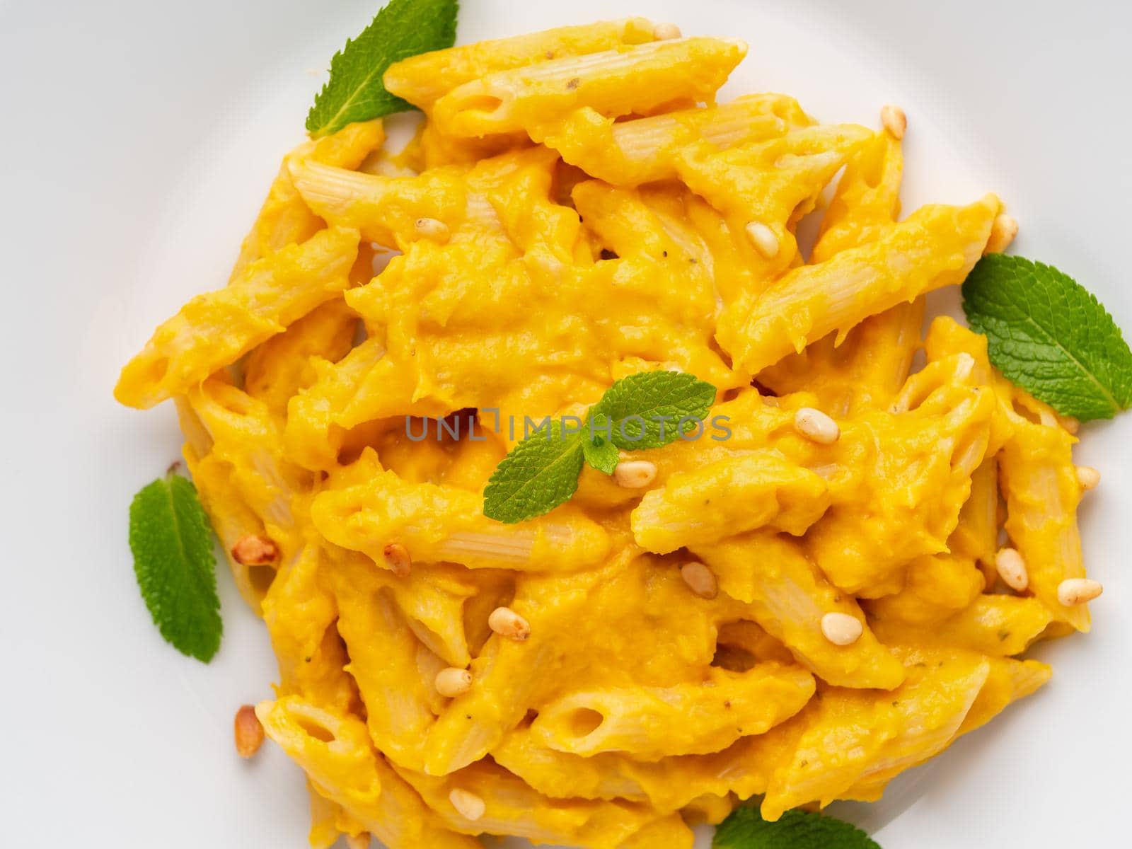 Pumpkin pasta penne with thick creamy sauce on white plate, top view, close-up