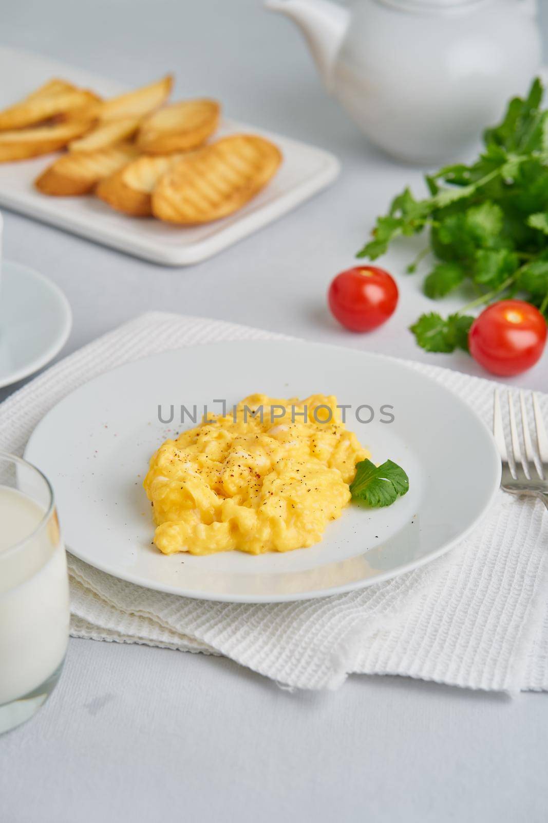 Scrambled eggs, omelet, vertical. Breakfast with pan-fried eggs, glass of milk, tomatoes on white background.