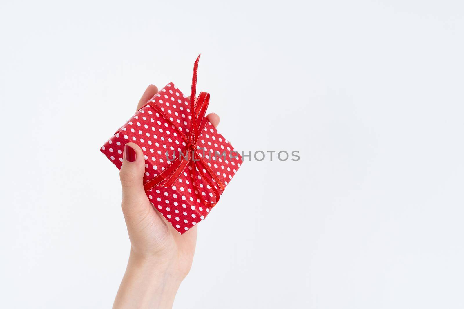 beautiful woman hands holding a red present with ribbon, hands with red nail polish gloss shine, concept on white background copy space