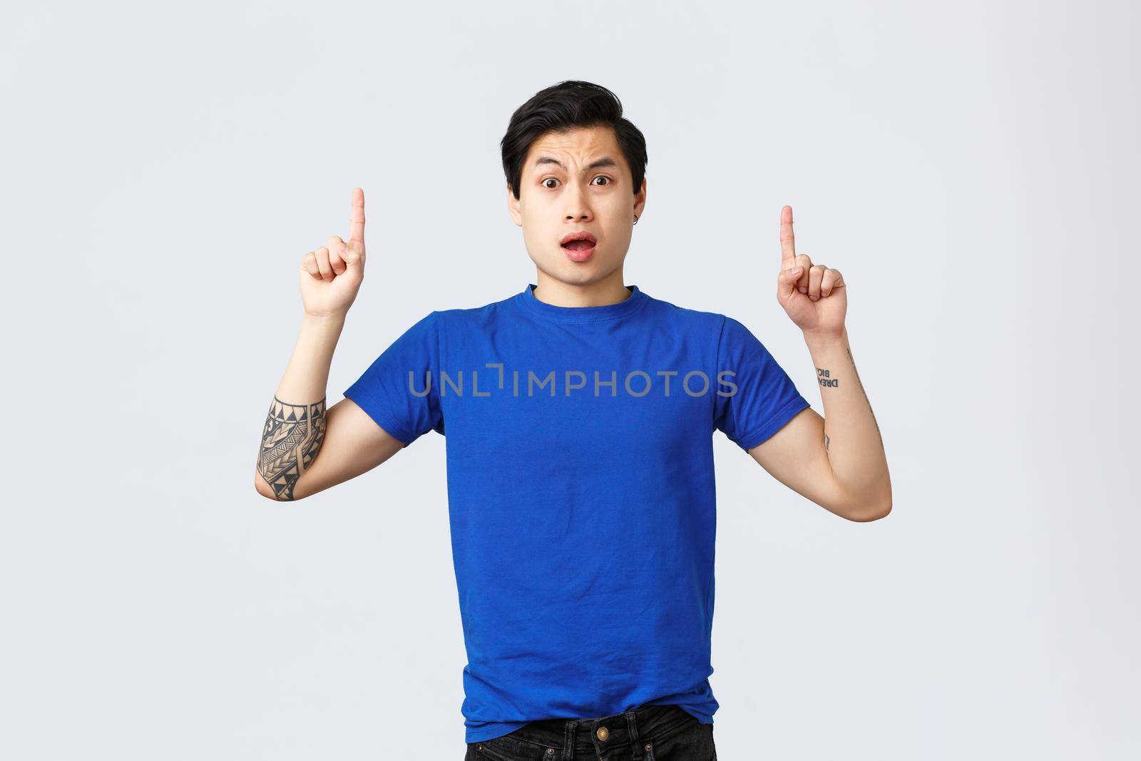 Different emotions, people lifestyle and advertising concept. Concerned and frustrated young asian man cant understand what happened, look confused and pointing fingers up, grey background.