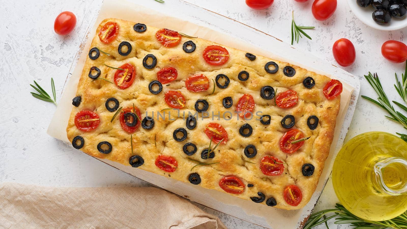 Focaccia with tomatoes, olives and a rosemary, top view. Italian flat bread, bottle with oil