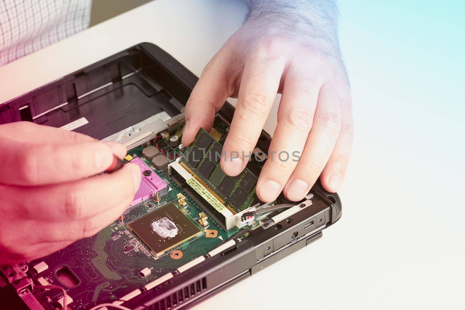 Man repairs computer. A service engineer in a shirt repairs a laptop, at a white Desk against a white wall, hands close up