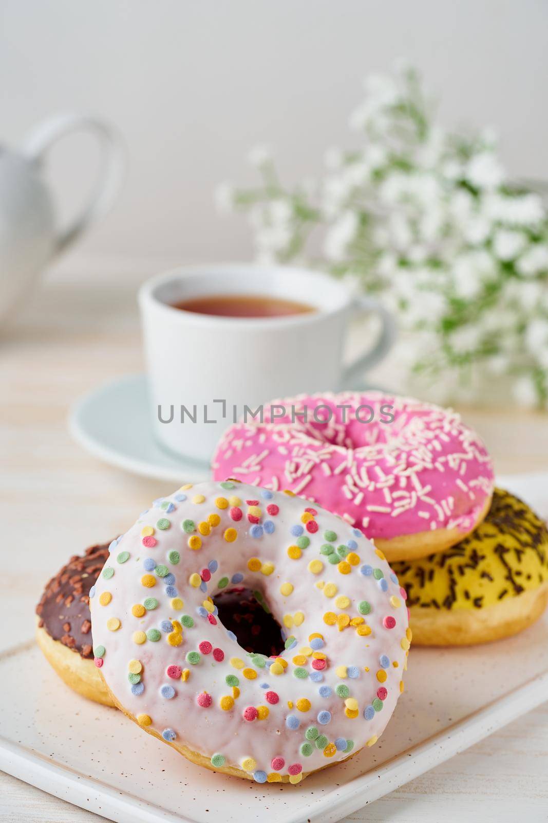 Doughnuts and tea. Bright, colorful junk food. Vertical. Light beige wooden background. Side view, close up.