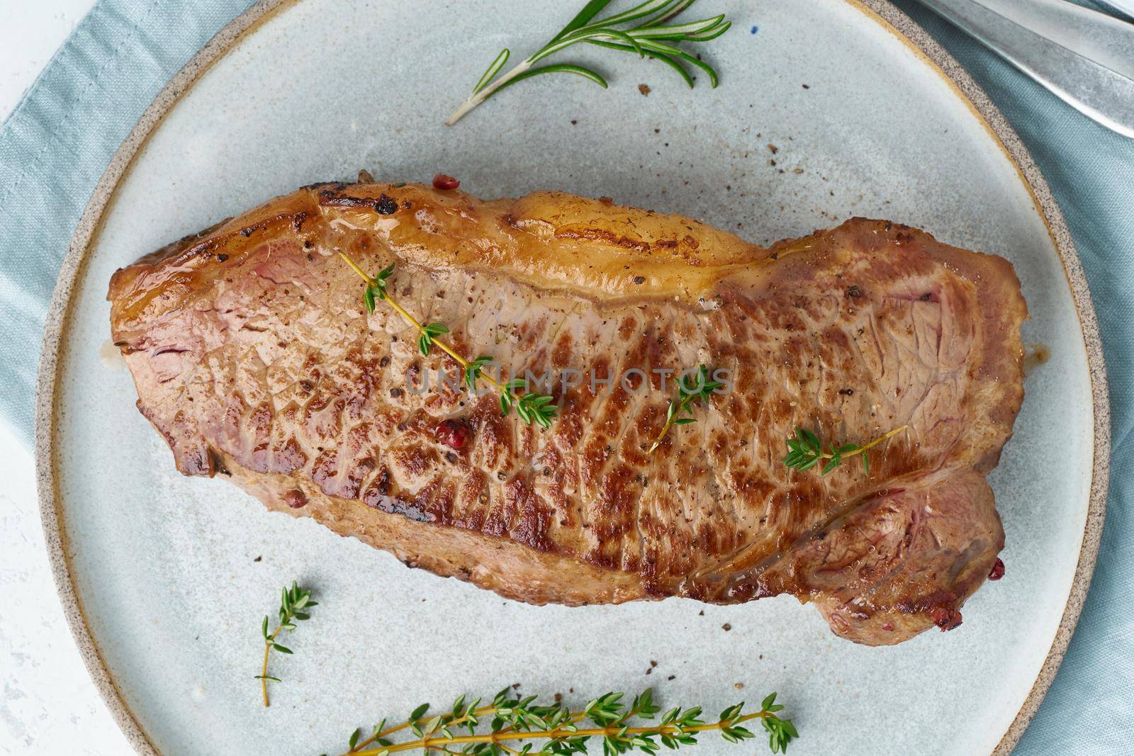 Keto ketogenic diet beef steak, striploin on gray plate on white background. Paleo food recipe with whole big piece of meat and seasoning. Macro, close up, top view, banner