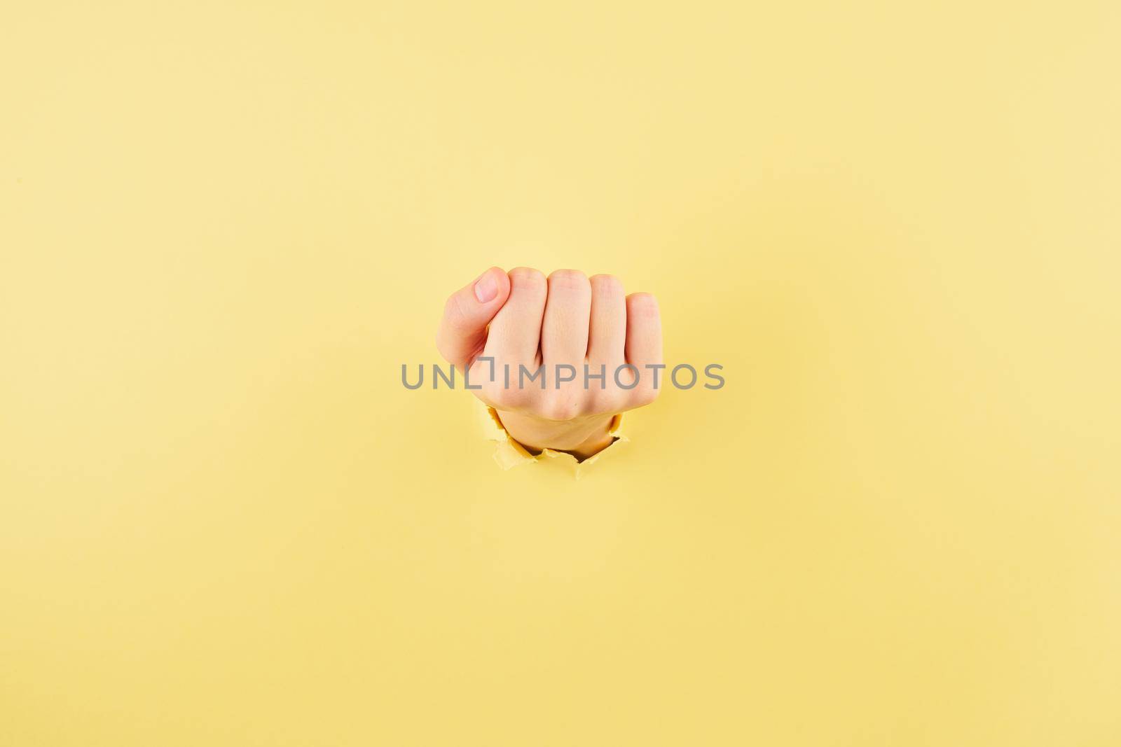 Woman showing her fist from the bursted hole on yellow cardboard background by NataBene