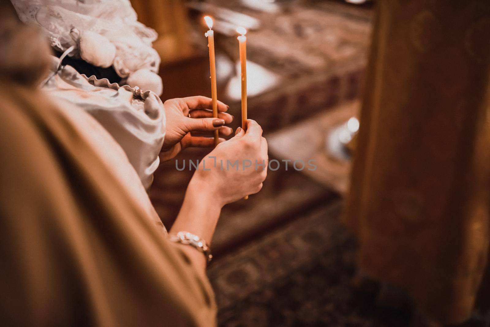 Female hands hold two burning candles in the church.