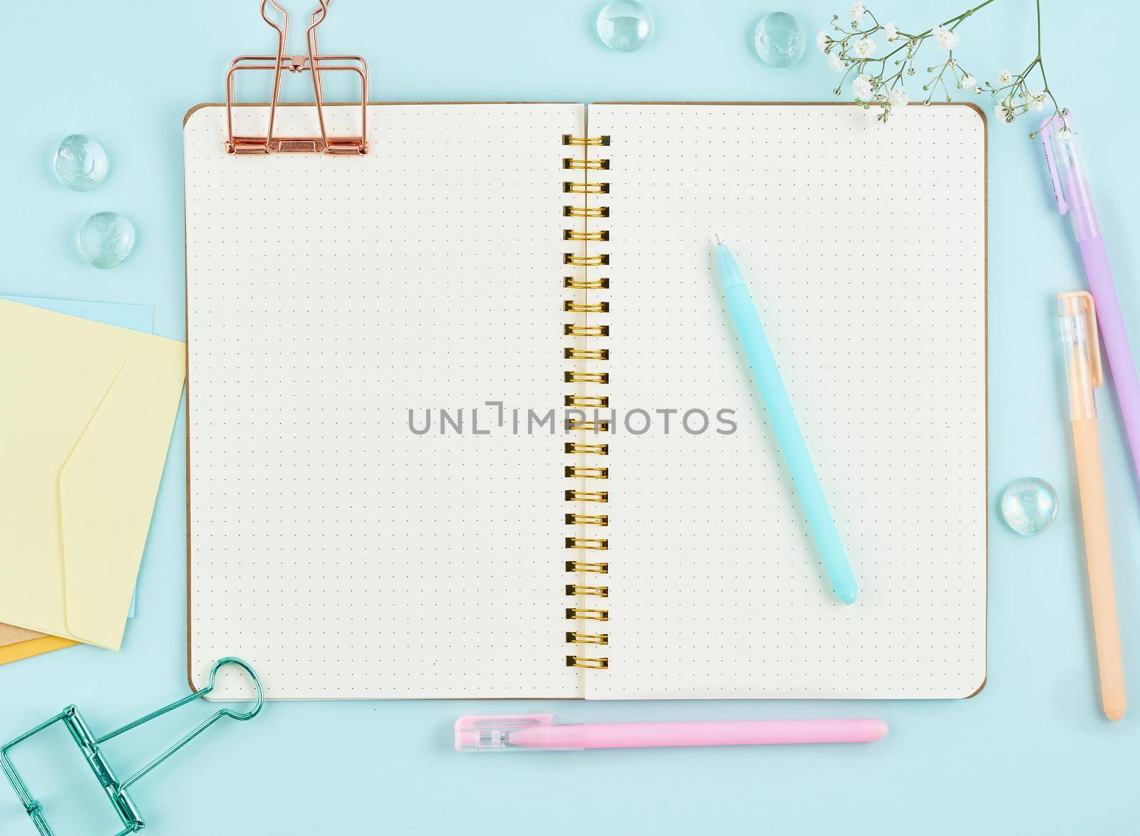 Blank notepad page in bullet journal on blue office desktop. Top view of modern bright table with notebook and flower. Mock up, copy space.