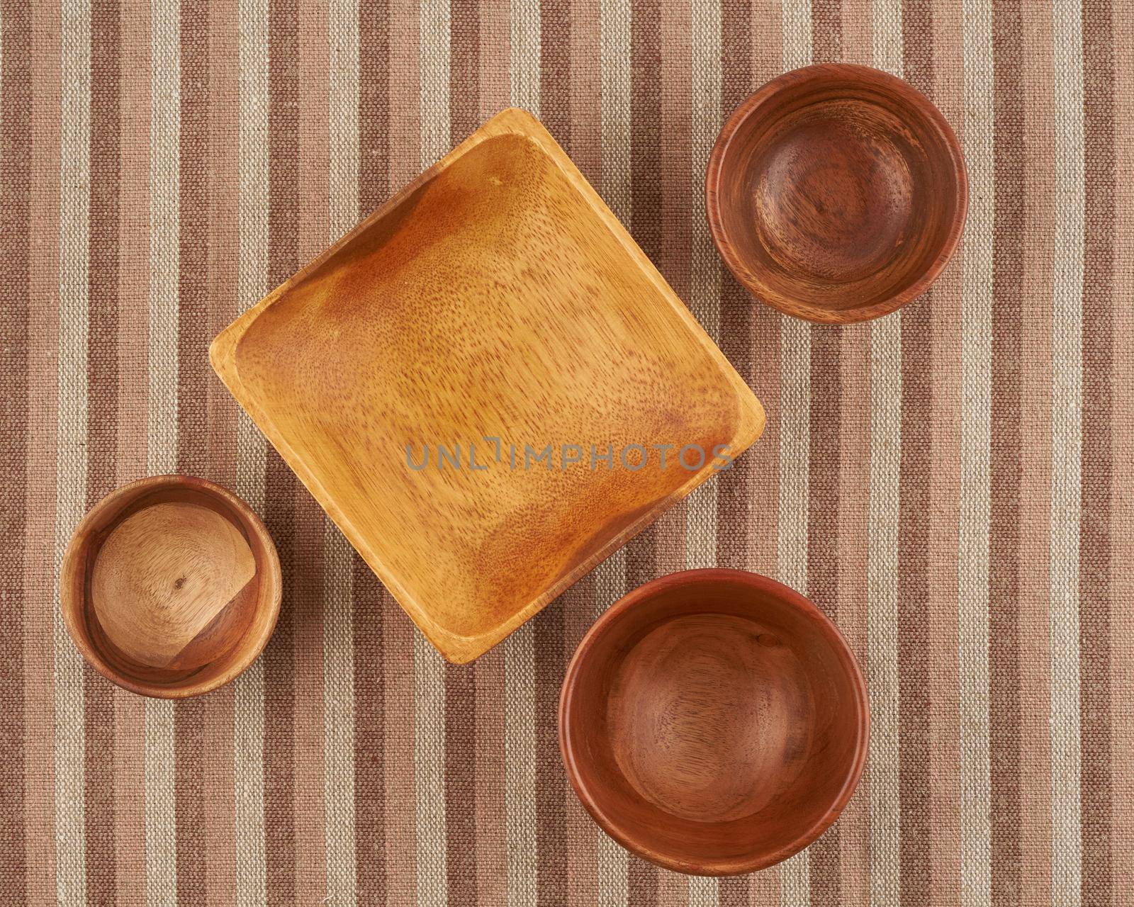 Wooden bowl on brown linen napkin, round and square shape, top view