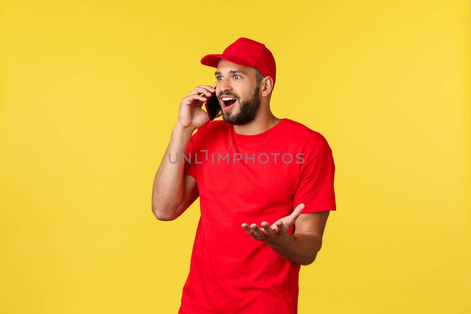 Contactless payment, online delivery, internet shopping and parcel tracking concept. Surprised and excited guy hear fantastic news over phone, wearing red cap and t-shirt, have mobile conversation.