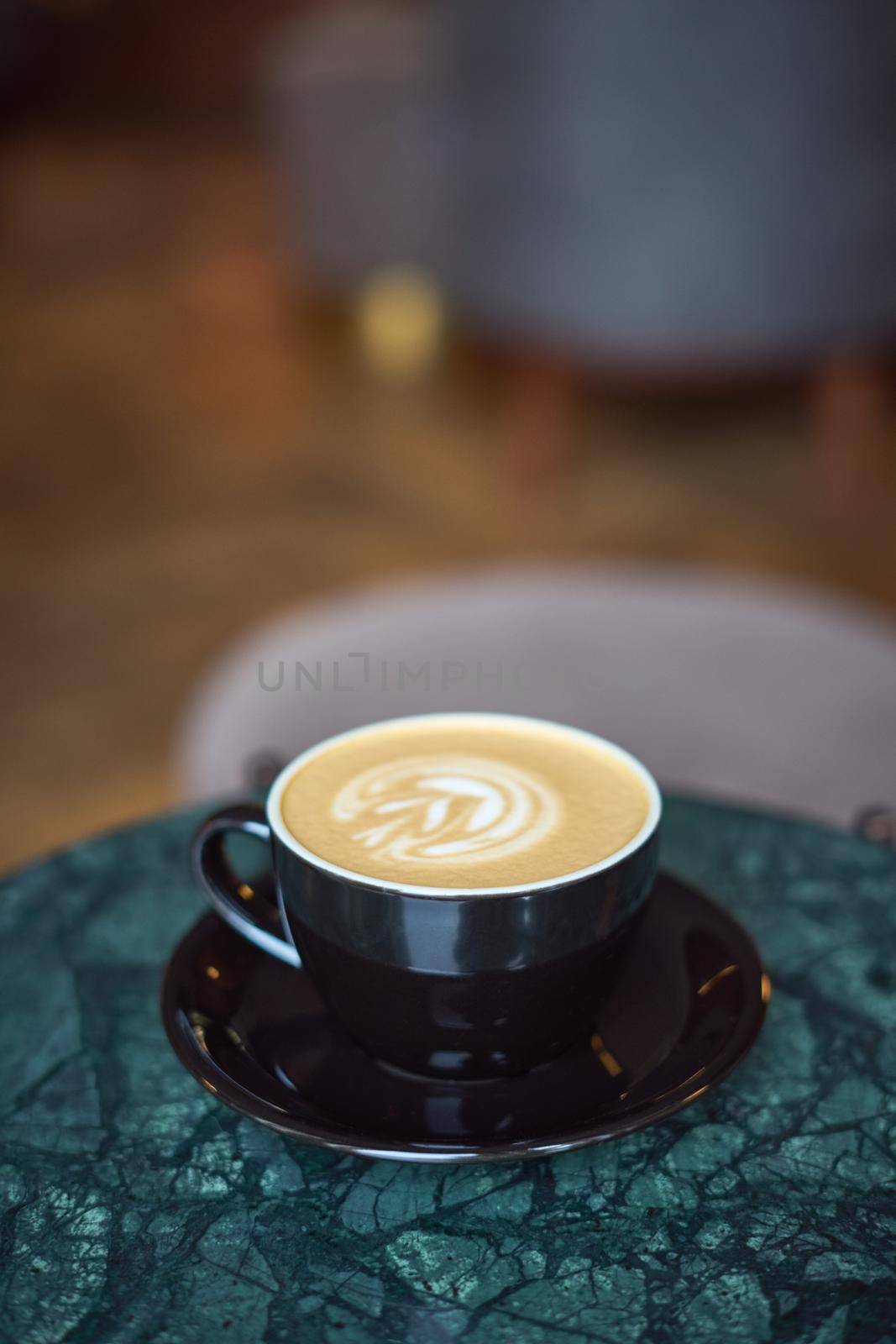 A Cup of cappuccino with foam on a marble table in a cozy little cafe. Drink by NataBene