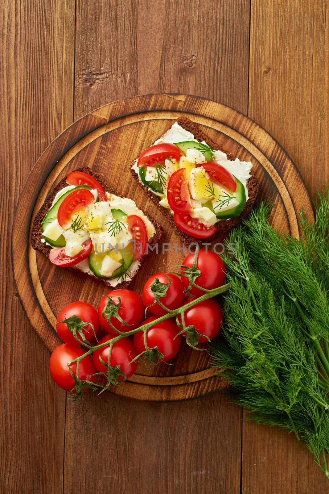 Smorrebrod - traditional Danish sandwiches. Black rye bread with boiled egg, cream cheese, cucumber, tomatoes on dark brown wooden background, top view