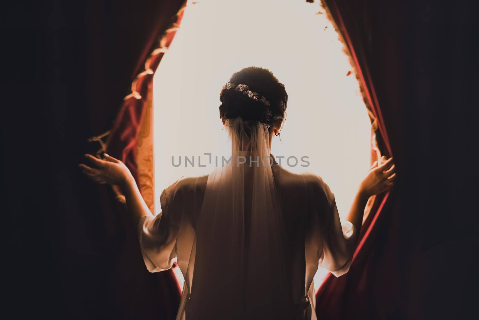 The bride opens the curtains on the huge white window. Girls on a white veil head.