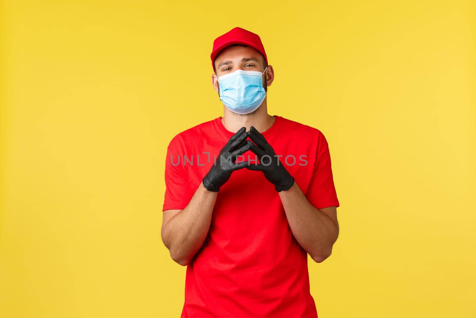 Express delivery during pandemic, covid-19, safe shipping, online shopping concept. Smart and creative courier in red uniform, gloves and medical mask, scheming, steeple fingers sly.
