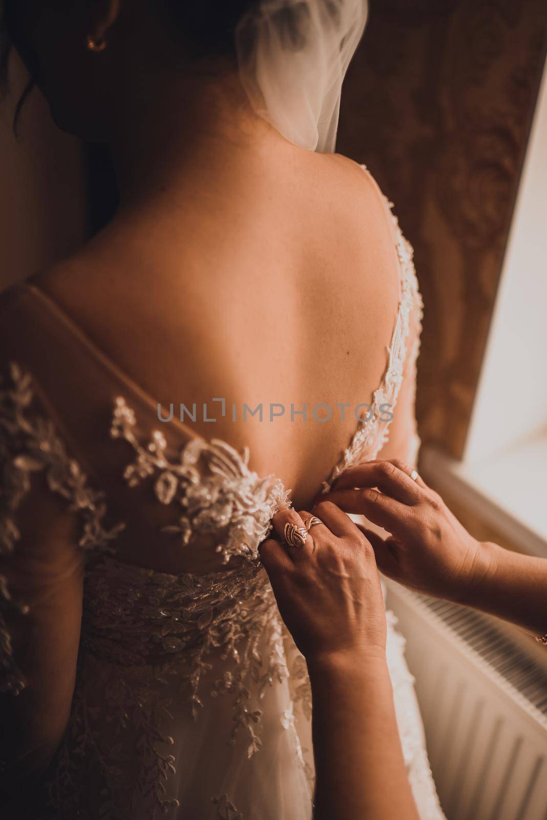 The back of the bride in a wedding dress. Mom's and woman's hands help fasten the clasps at the back.
