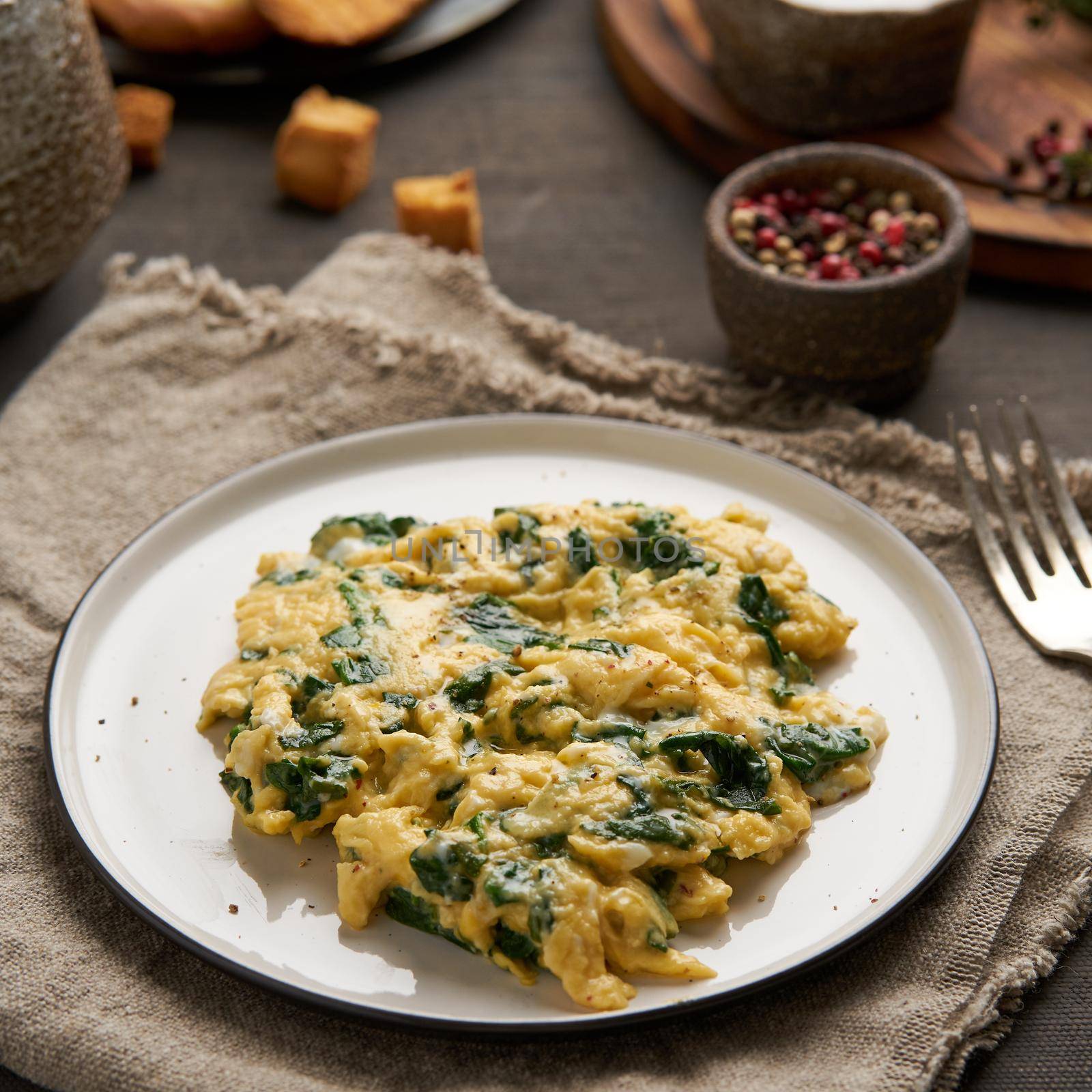 Scrambled eggs with spinach, cup of tea on dark brown background. Breakfast with Pan-fried omelette, side view, close up