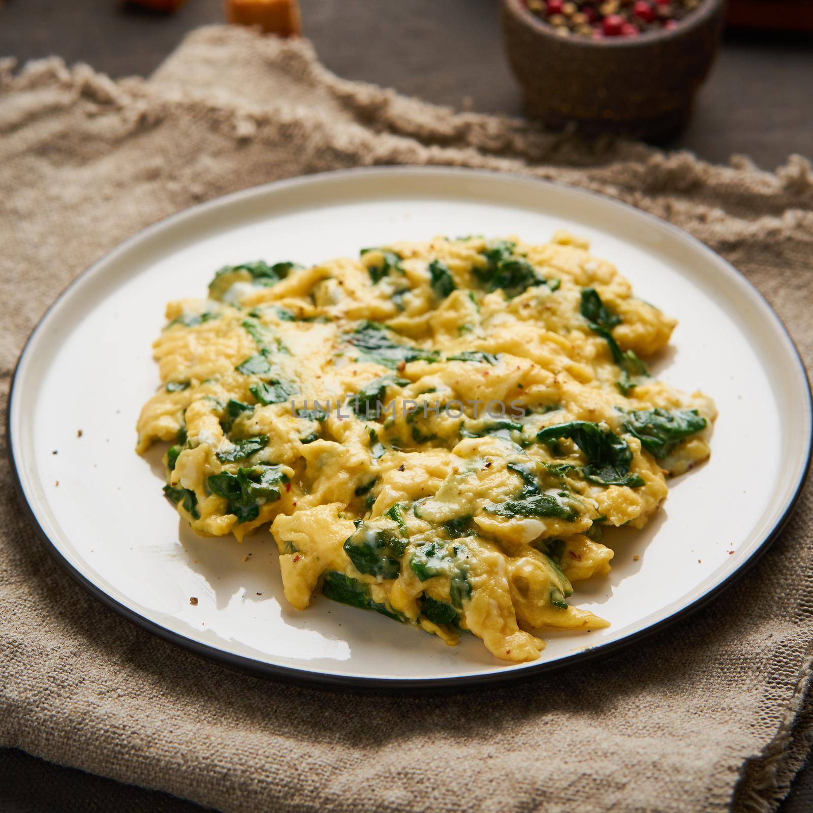 Scrambled eggs with spinach, cup of tea on dark brown background. Breakfast with Pan-fried omelette, side view