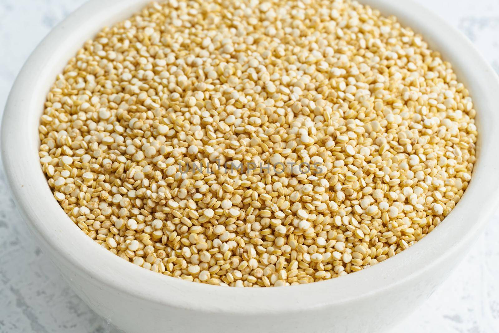 Quinoa seed in a white bowl on white background. Dried cereals in cup, vegan food, fodmap diet. Side view, close up.