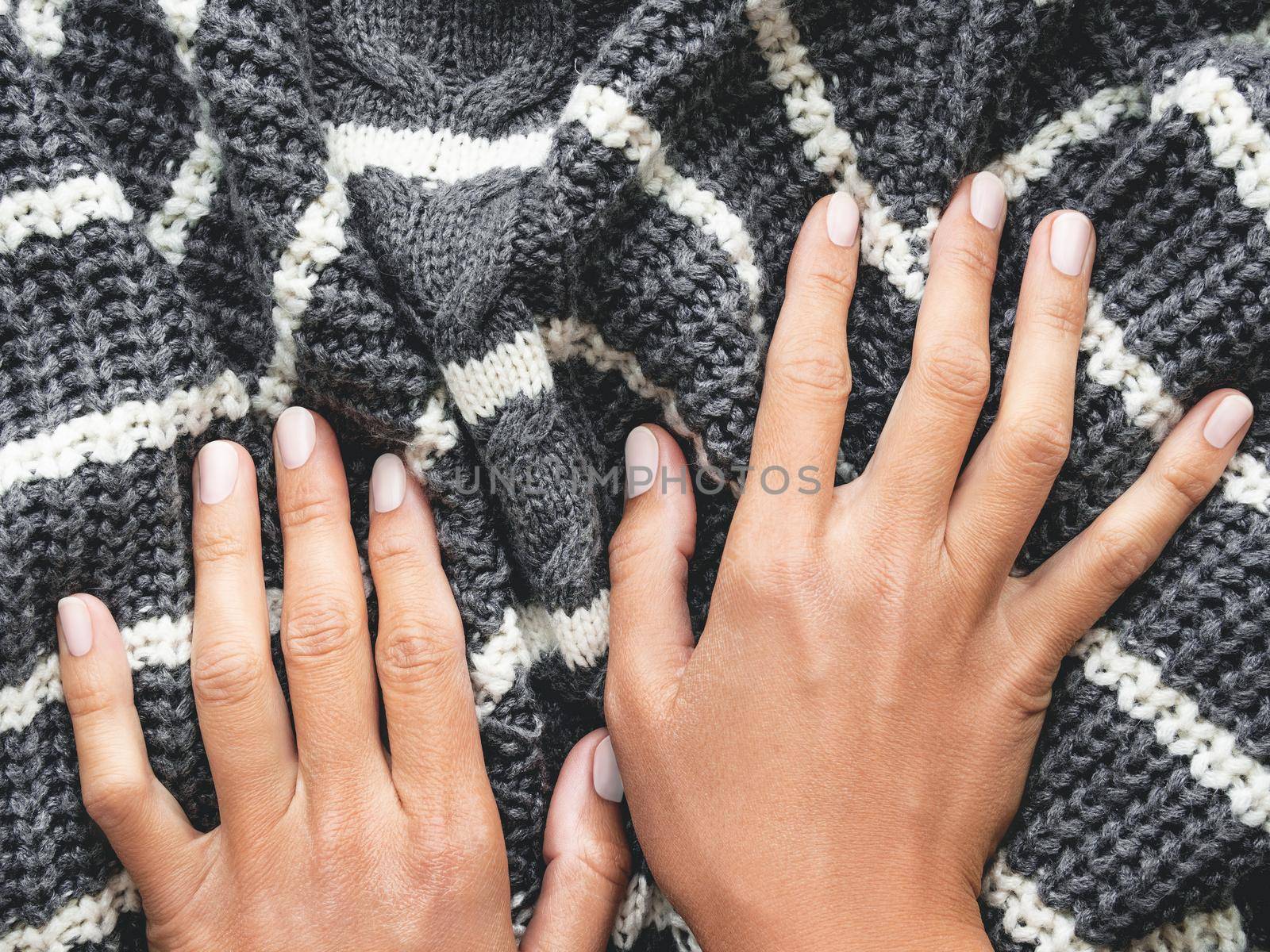 Woman's hands on gray knitted sweater with white stripes. Folded warm clothing. Crumpled textile background.