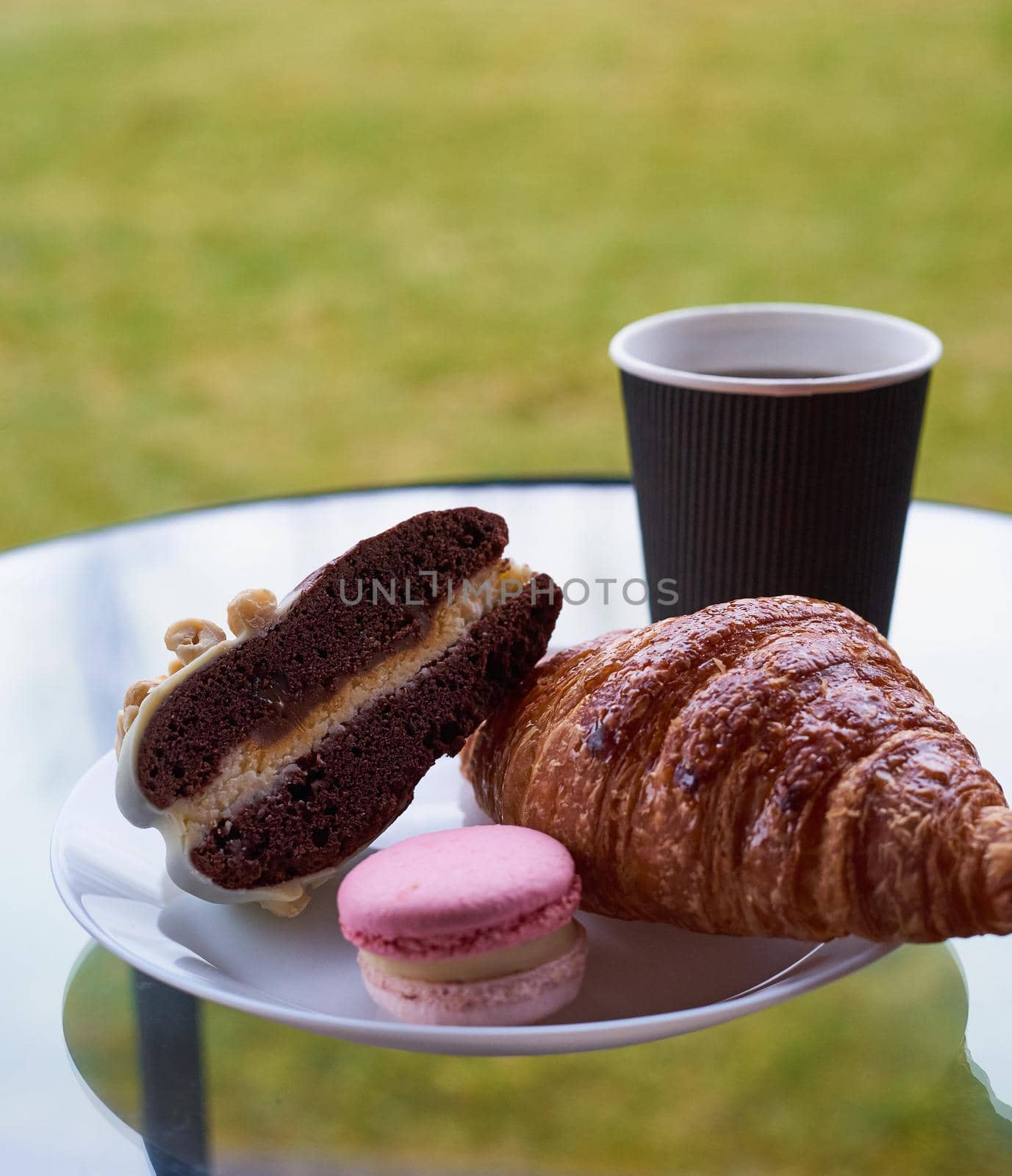 Breakfast with croissant and dessert, coffee or tea in plastic mug, in the village, outdoors, nature. Selective focus. Vertical