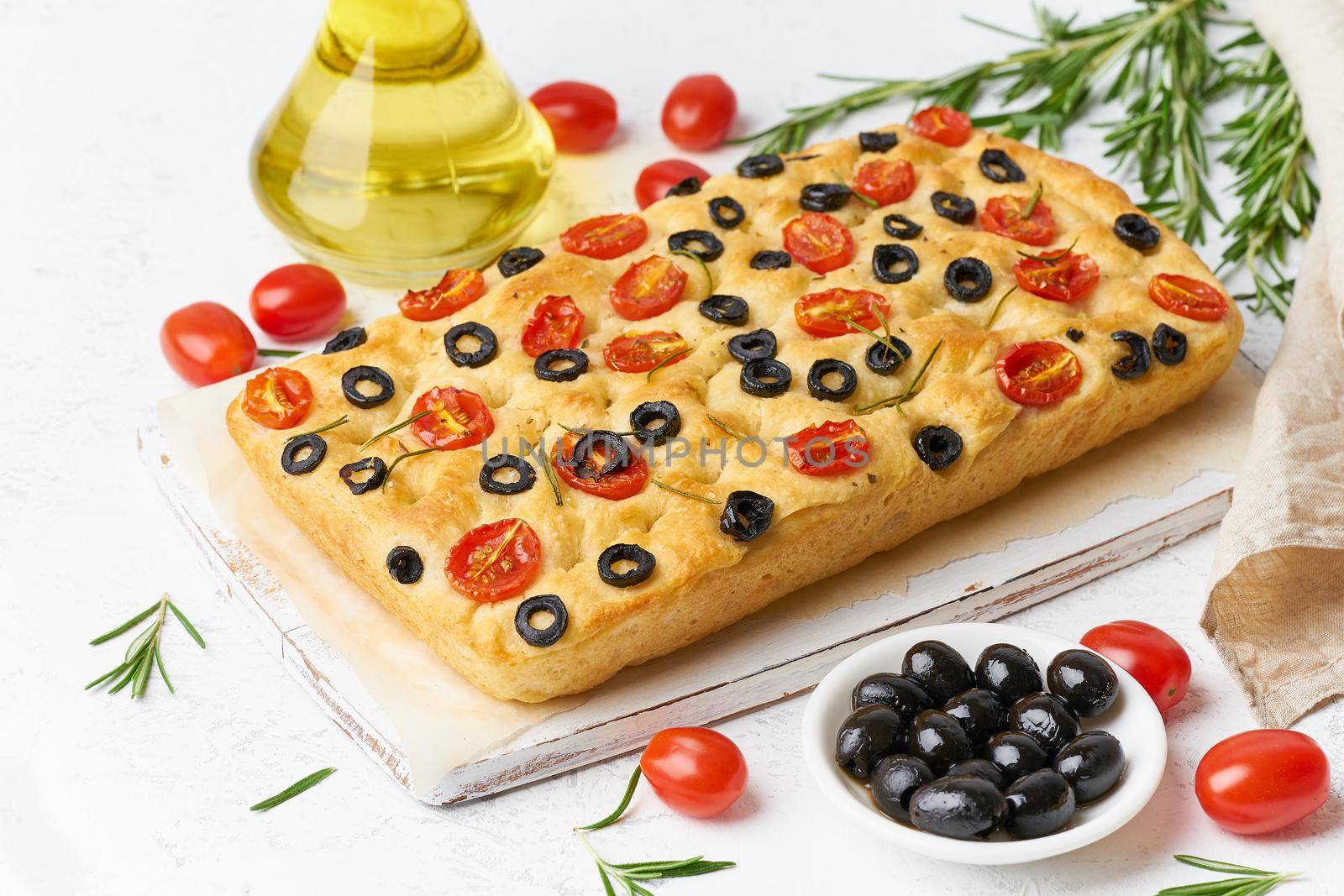 Focaccia with tomatoes, olives and rosemary. Whole Italian flat bread, bottle with oil by NataBene