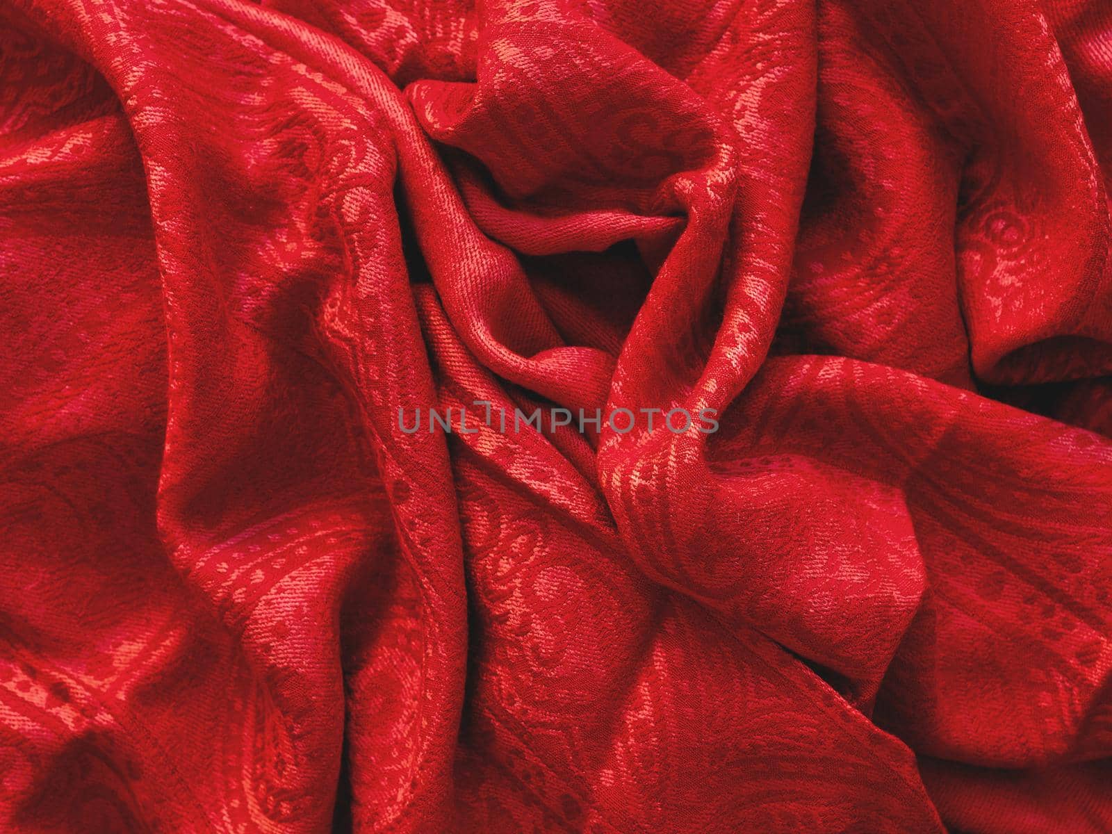 Bright red scarf. Folded warm accessory. Crumpled textile background with ornament. Top view on fabric backdrop.