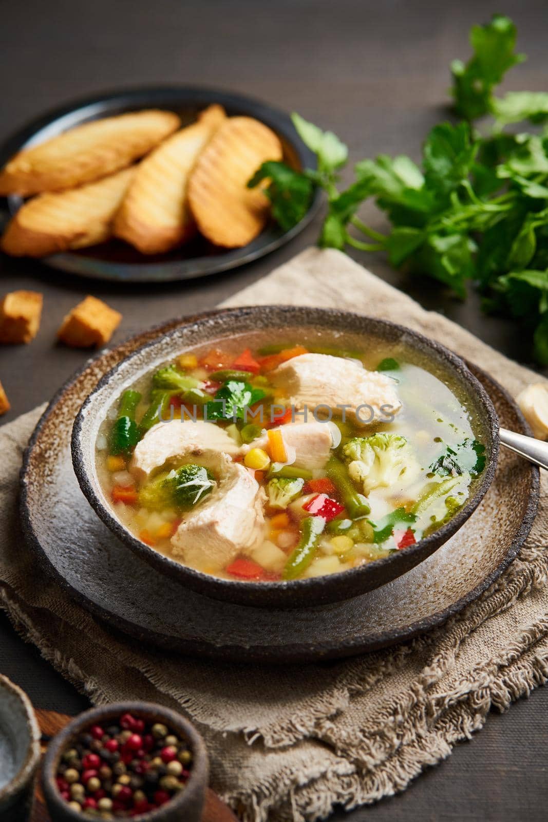 Homemade chicken soup with vegetables, broccoli on dark brown background, vertical, side view.