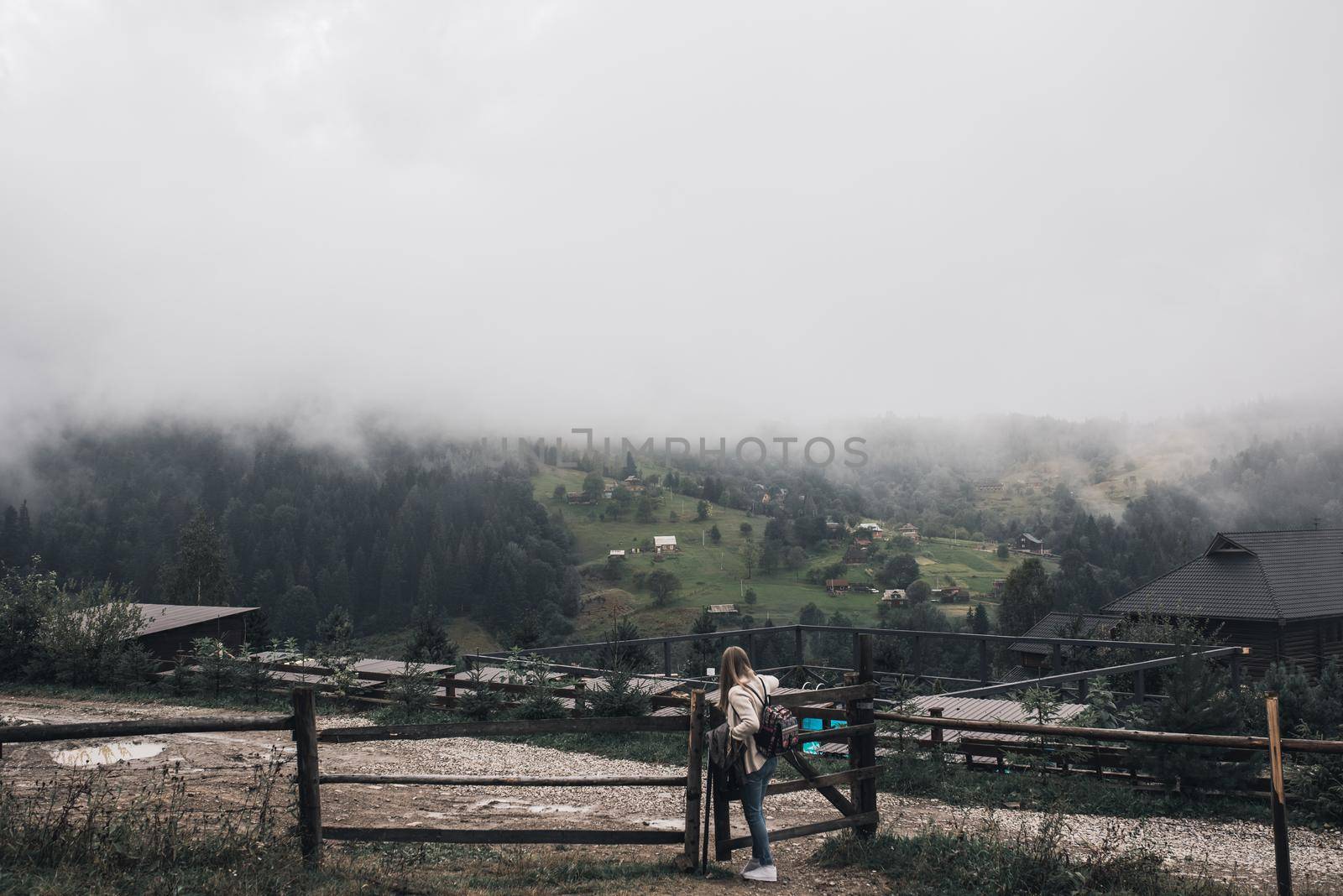 woman traveler near old fence against Carpathian mountains in fog by AndriiDrachuk