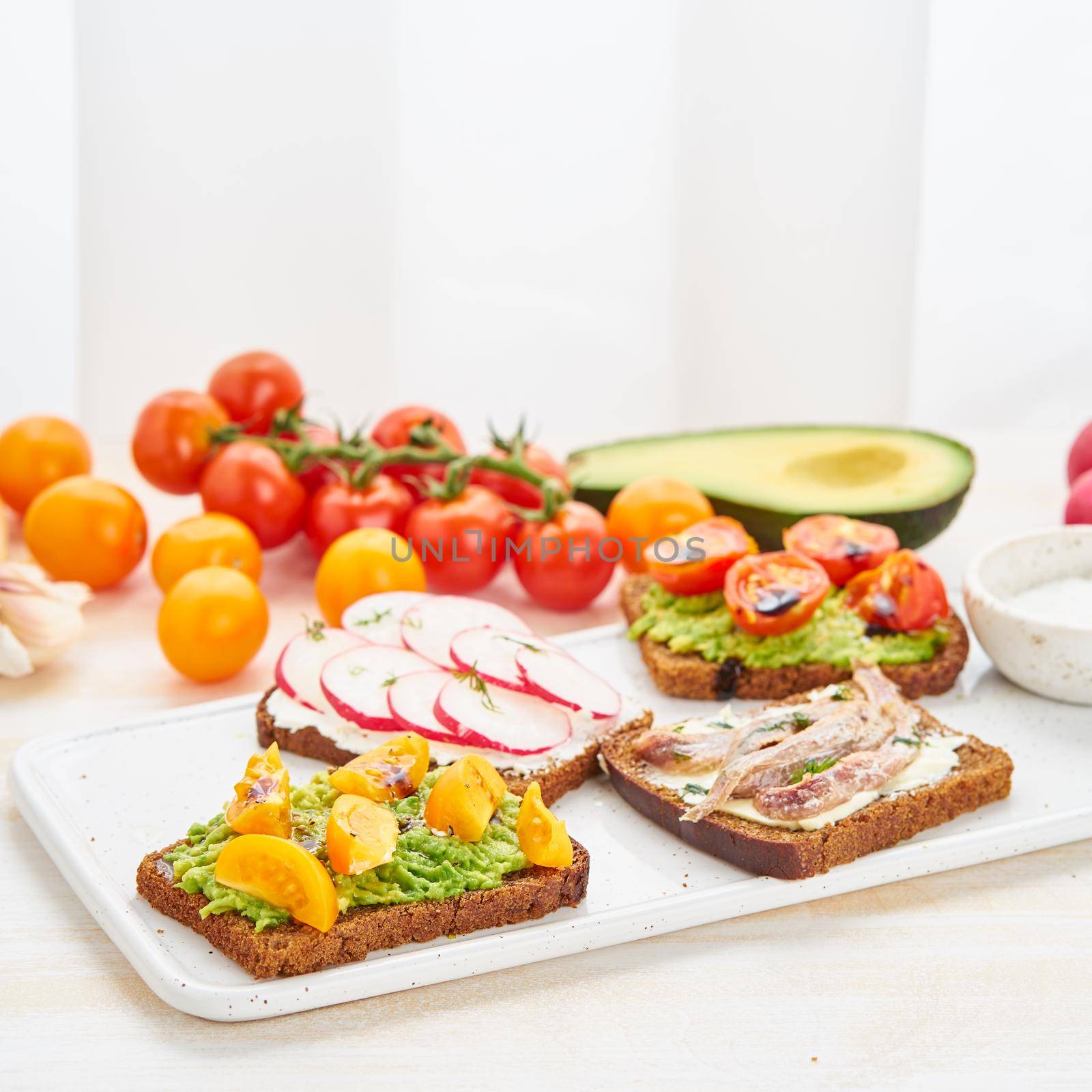 Set of smorrebrods with fish, anchovies, avocado, tomatoes, radish. Side view, copy space, white background.