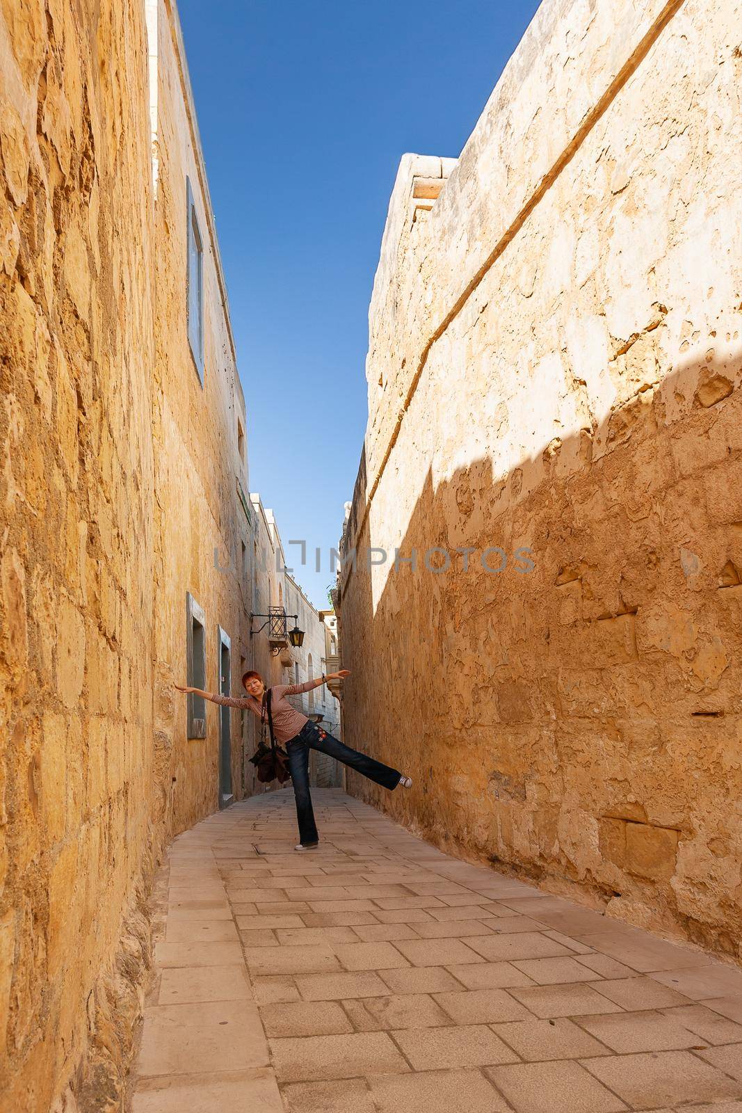 MDINA, MALTA - February 18, 2010. Tourist woman is showing how narrow is street of Mdina, old capital of Malta. by aksenovko