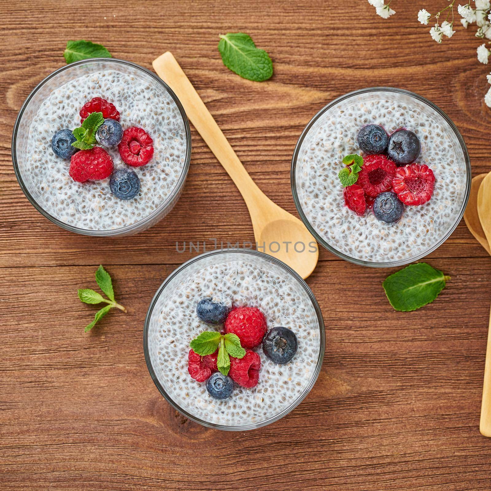 Chia pudding with fresh berries raspberries, blueberries. Top view, three glass on brown wooden background, close up.