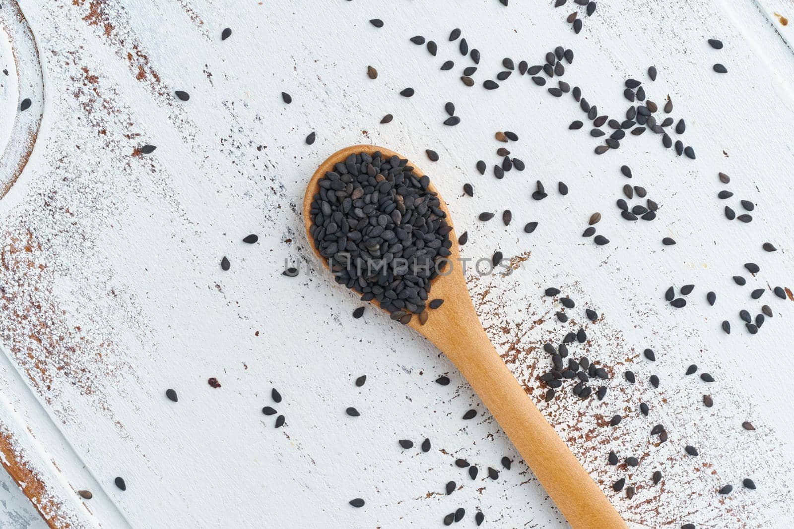 Black Sesame on a wooden spoon. White wooden background. Top view, close up. Copy space.