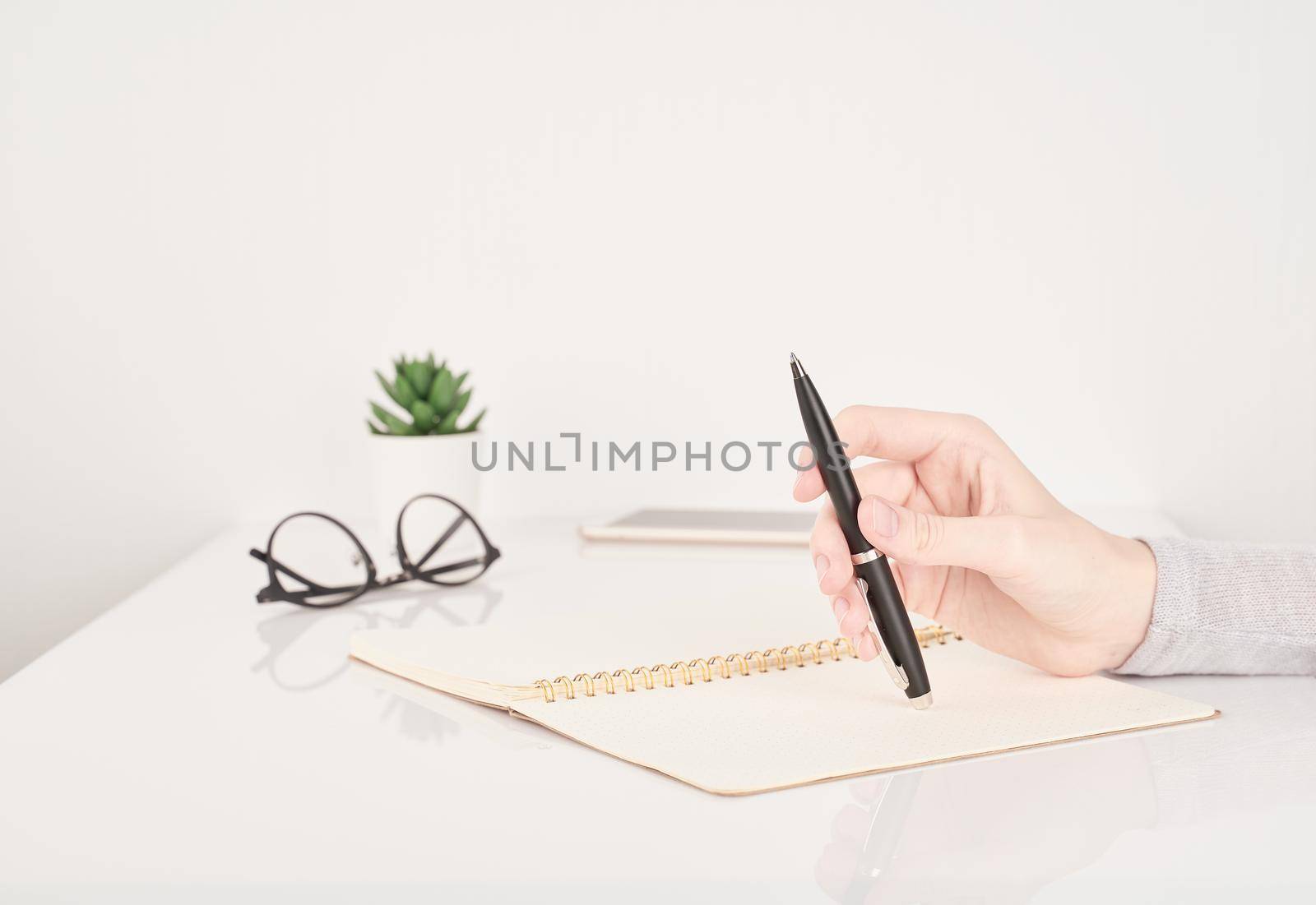 female young hand holding pen and writing on notebook page on white and gray background side view copy space