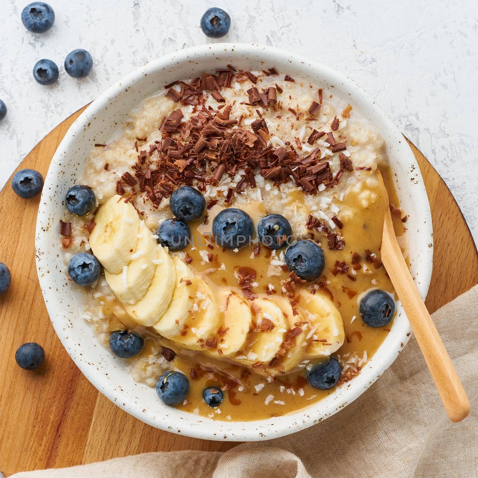 Oatmeal rustic porridge with blueberry, bilberry, blackberry, banana, chocolate and nut honey pasta, dash diet, wooden white background top view