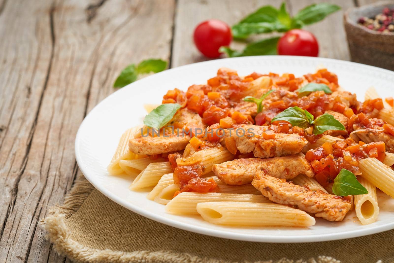 Penne pasta, chicken or turkey fillet, tomato sauce with basil leaves on old rustic wooden background. Copy space, side view, close up