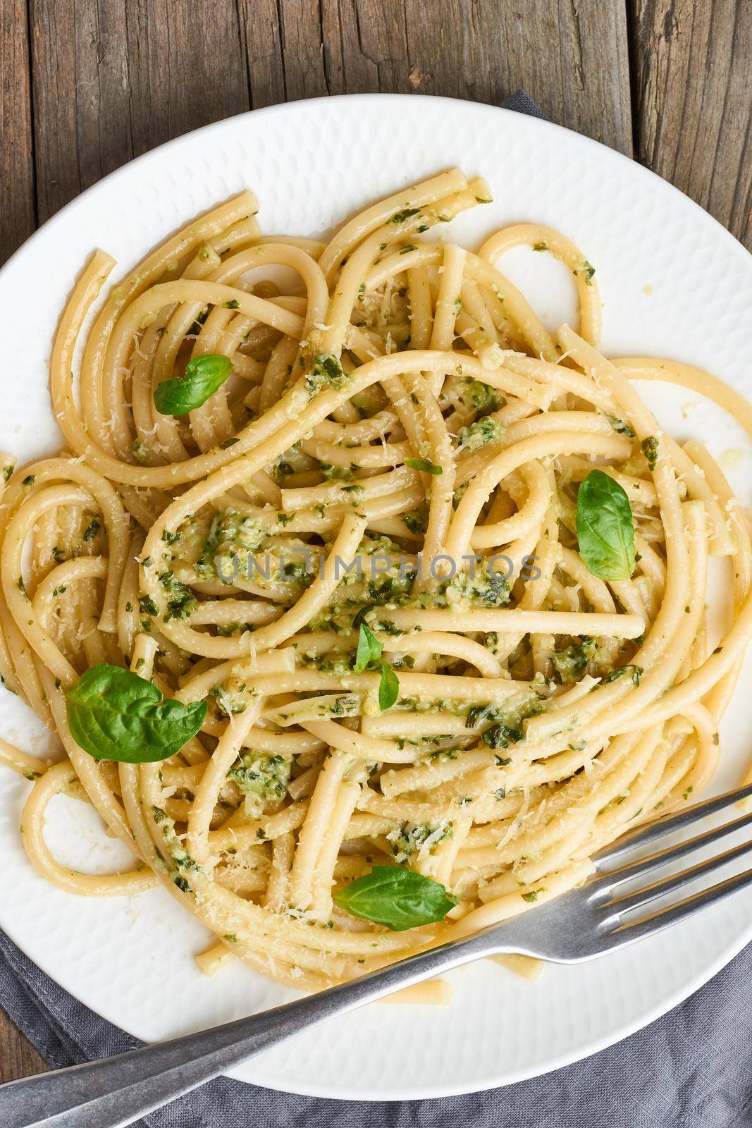 Pesto spaghetti pasta with basil, garlic, pine nuts, olive oil. Vertical. Rustic table by NataBene