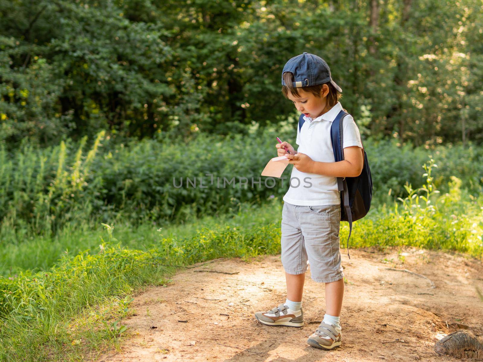 Mindful boy writes something in notebook while walking in forest. Exploring nature. Summer outdoor recreation. Healthy lifestyle.