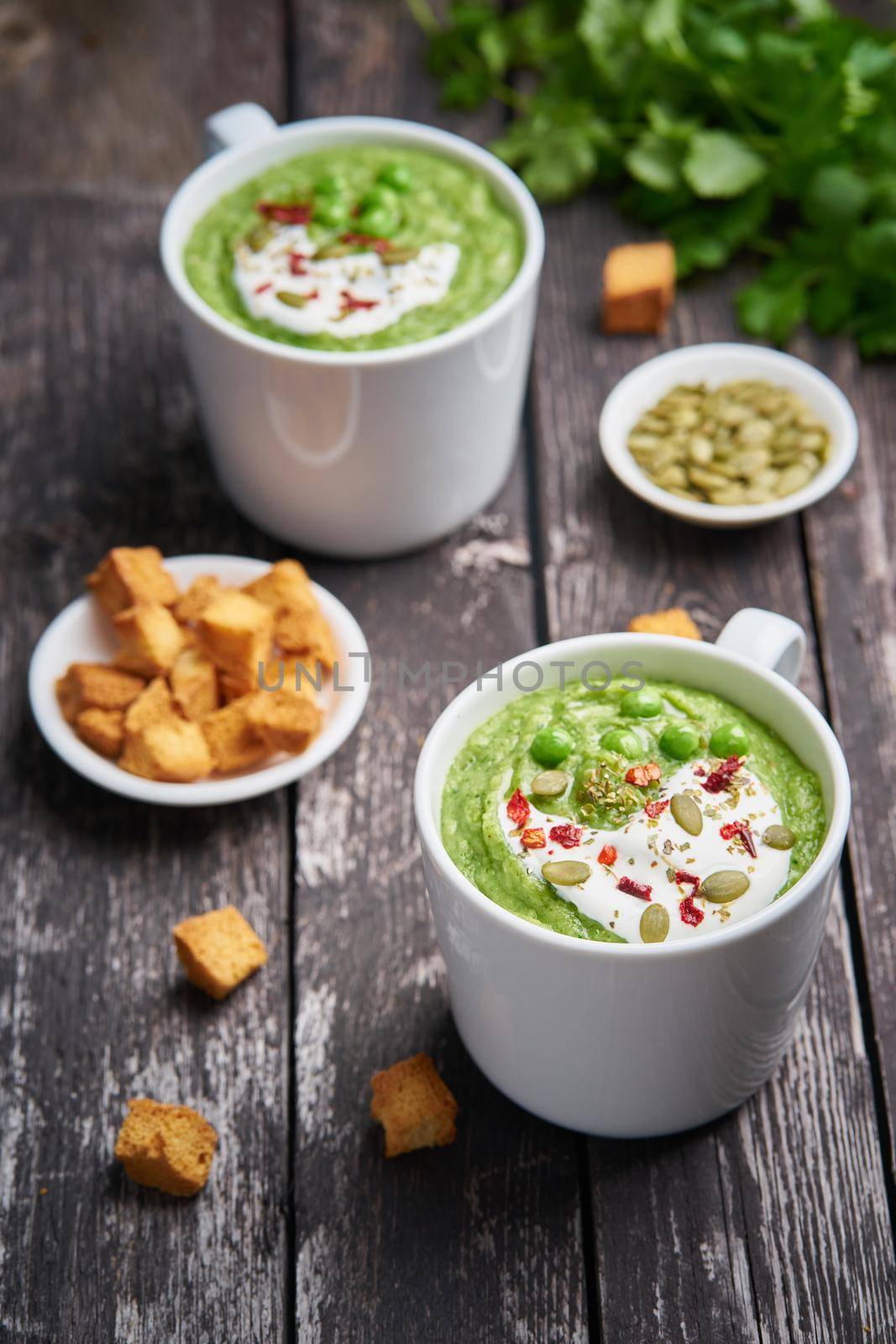 Broccoli cream soup, vertical. Vegetable green puree in two large white cup. Diet vegan soup of broccoli, zucchini, green peas on dark wooden background.