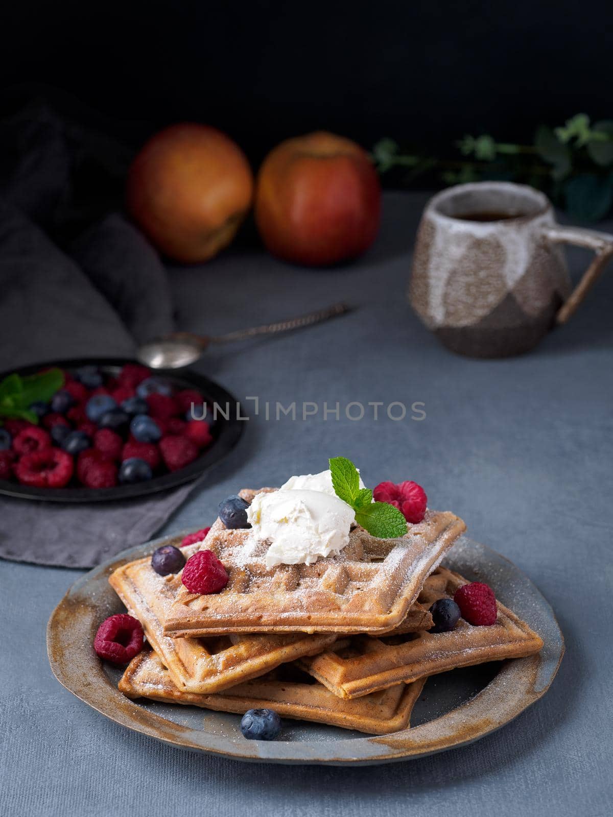 Belgian waffles with raspberries, chocolate syrup. Breakfast with tea on dark background, side view, vertical