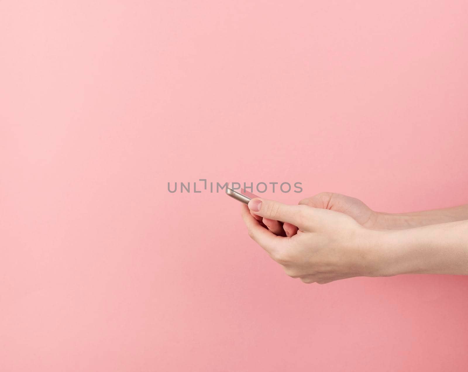 woman hand without manicure hold phone on pastel pink background with copy space