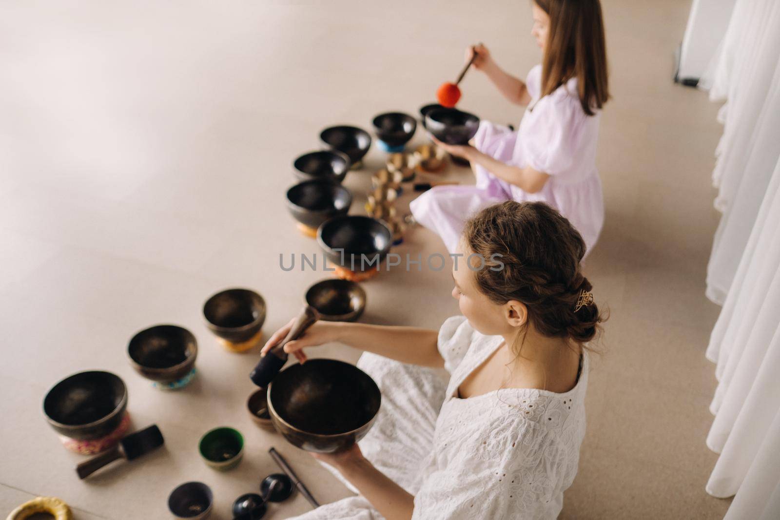 Two female yoga teachers play on Tibetan bowls in the gym during a yoga retreat by Lobachad
