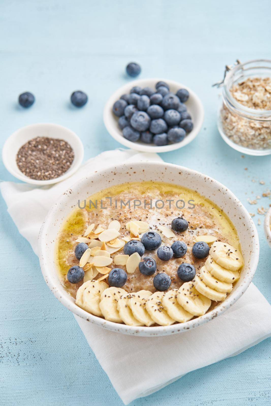 Oatmeal with blueberries, banana on blue light background. Side view, vertical. Healthy diet breakfast