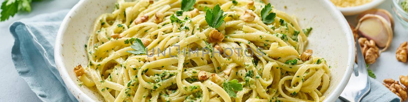 Banner with pesto pasta, bavette with walnuts, parsley, garlic, nuts, olive oil. Side view, long side, blue background