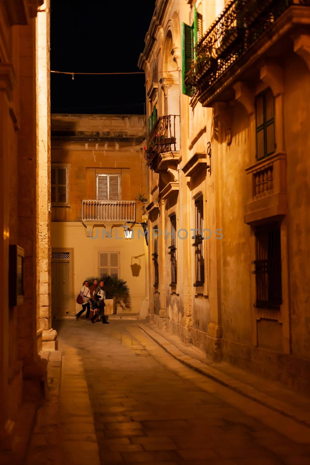 MDINA, MALTA - February 19, 2010. Tourists on illuminated streets of Mdina, ancient capital of Malta. Night view on buildings and wall decorations of ancient town. by aksenovko