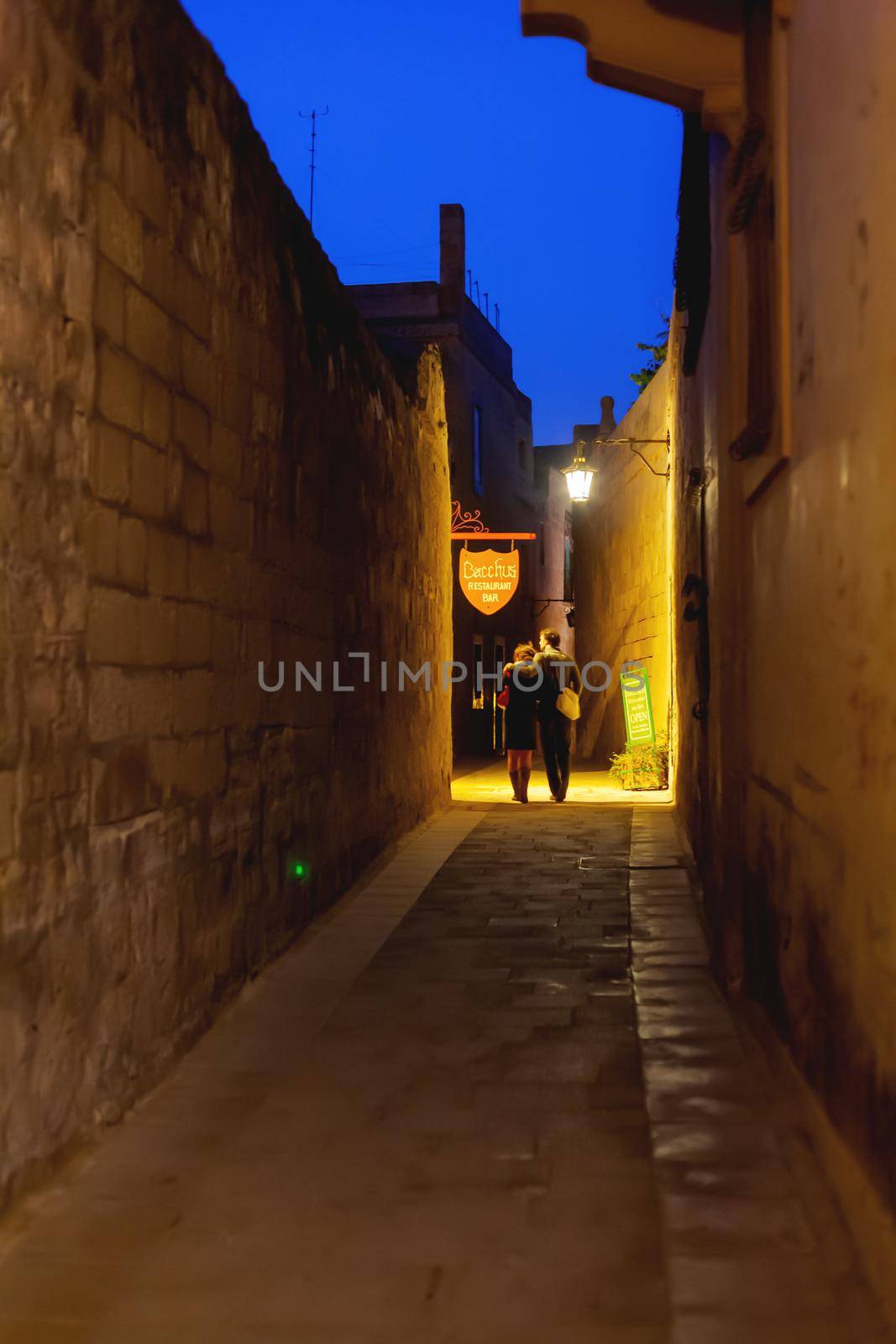MDINA, MALTA - February 19, 2010. People walking down narrow streets with cafes and restaurants. Night view on illuminated buildings and wall decorations of ancient town. by aksenovko
