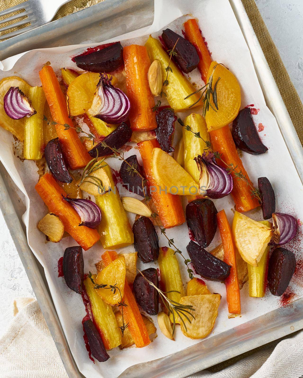 Colorful roasted vegetables on tray with parchment. Mix of carrots, beets, turnips, rutabaga, onions. Vegetarianism, veganism, proper nutrition, lchf. Top view