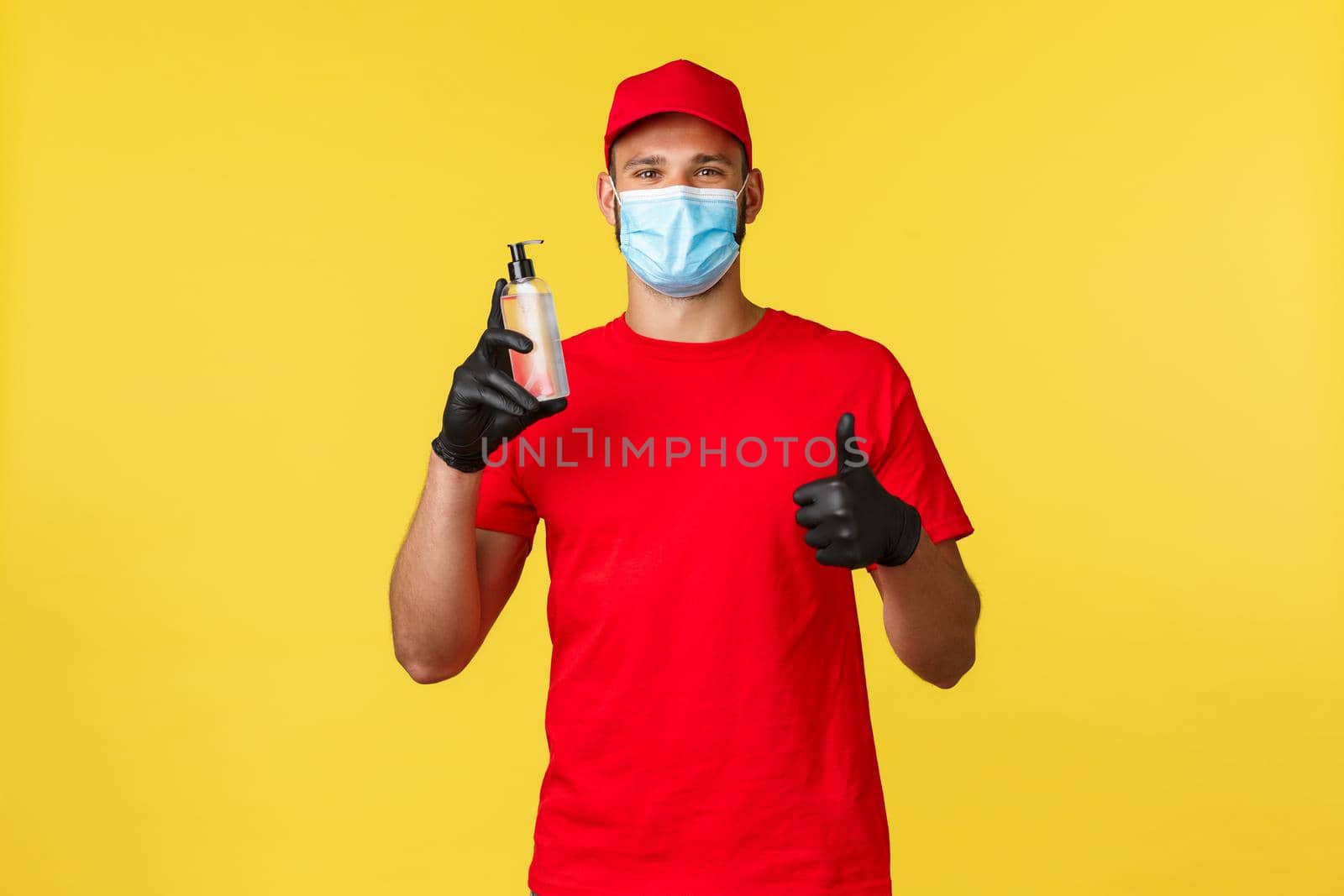 Covid-19, delivery orders, shopping, contactless handling and social distancing concept. Cheerful smiling courier in medical mask, gloves, show thumb-up, recommend hand sanitizer.
