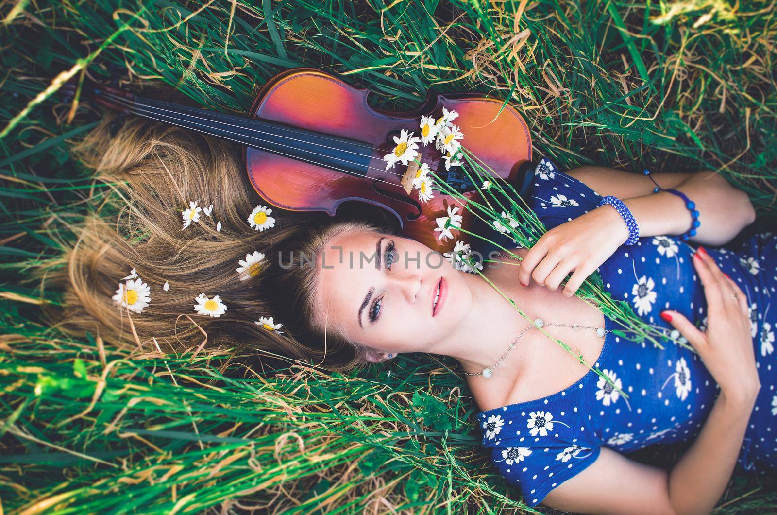 Young girl blonde lies in grass with violin. by AndriiDrachuk