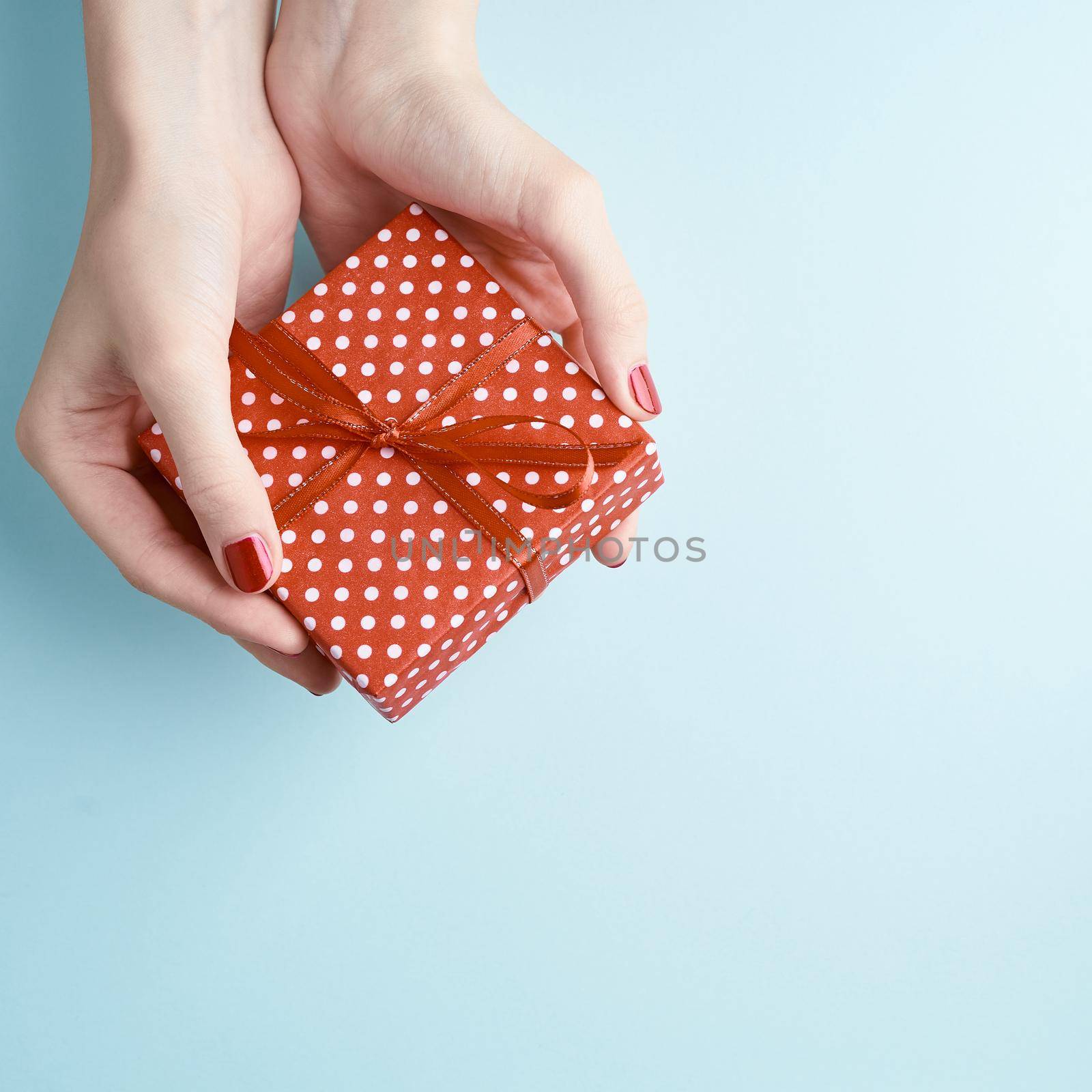 woman hands holding red gift with ribbon, manicured hands with nail polish by NataBene